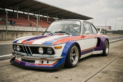 BMW 3.0 CSL en livrée Motorsport dans la voie des stands d'un circuit vintage européen, vue trois quarts avant