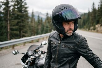 Motard équipé d'un casque Shoei intégral posant devant une route de montagne boisée