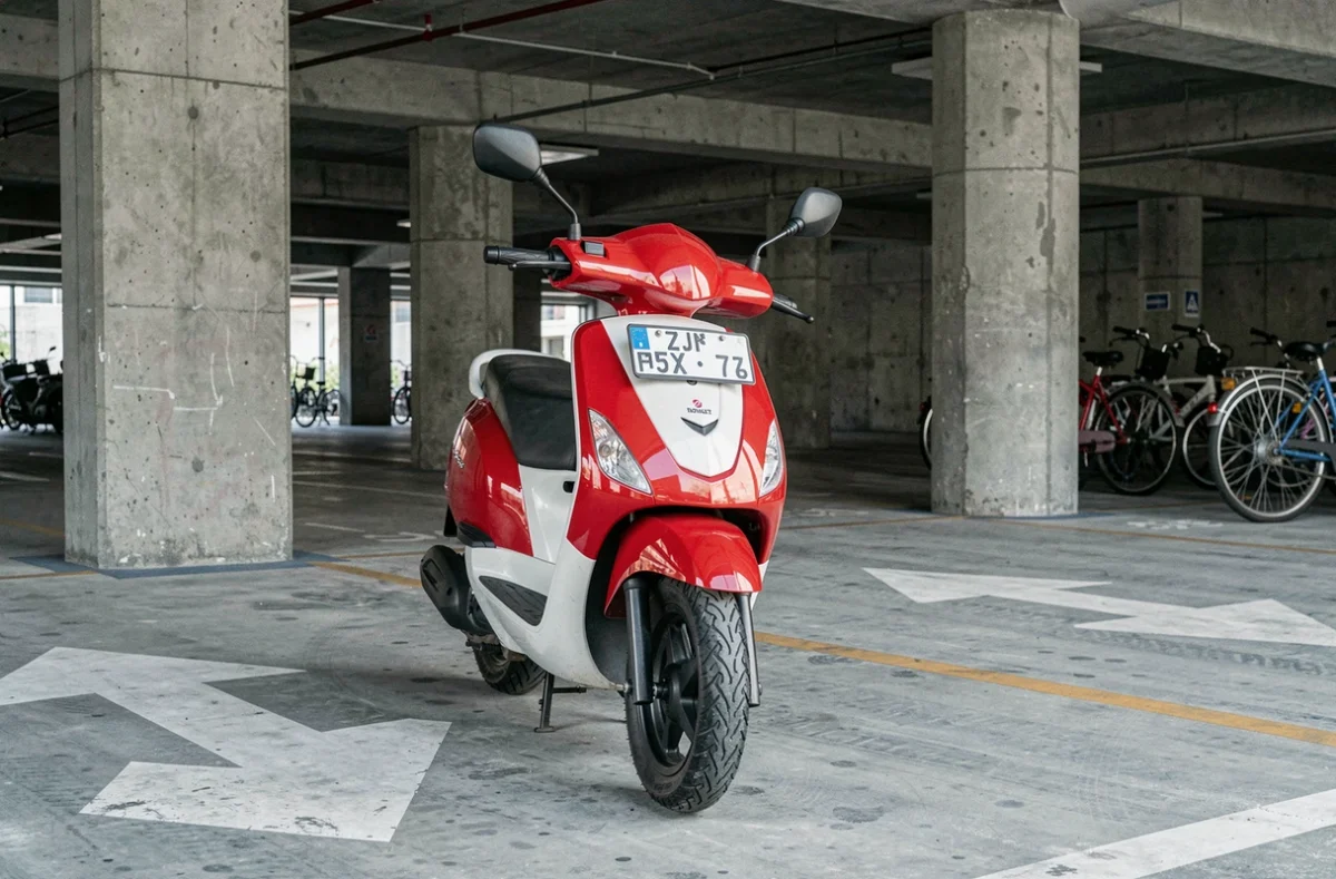Scooter 50cc rouge et blanc garé dans un parking urbain couvert illustrant les coûts d'assurance