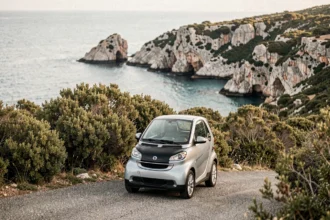Petite voiture sans permis garée sur une route côtière de Corse avec vue sur une crique méditerranéenne turquoise